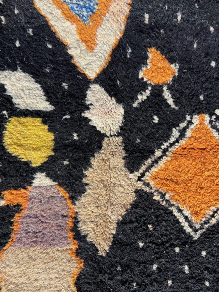 tapis berbère à motifs géométriques colorés sur fond noir, avec franges aux extrémités